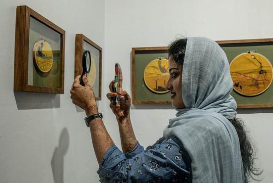 一位观众正在用放大镜观看并拍摄Bapi Das的作品